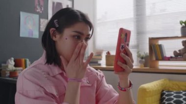 Burnunda mücevher bandajlı neşeli Z kızı, elinde çıkartma kaplı akıllı telefon ve modern rahat yatak odasında vlog çekerken rinoplasti hakkında konuşuyor.