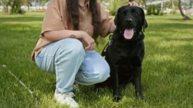 Parkta çimenlikte oturan siyah rehber köpeği okşayan görme engelli kızı yukarı kaldır.