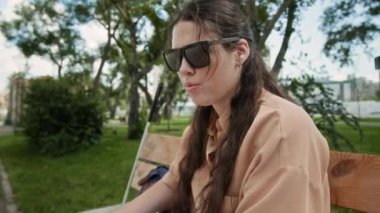 Siyah gözlüklü, parktaki bankta körler alfabesi kitabı okuyan görme engelli genç bir kadının bakışını eğ.