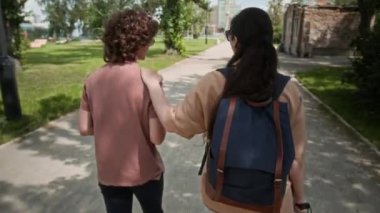 Parkta yürürken sohbet eden iki genç kadın, arkadaşlarının omzunda baston tutan görme engelli bir kız.