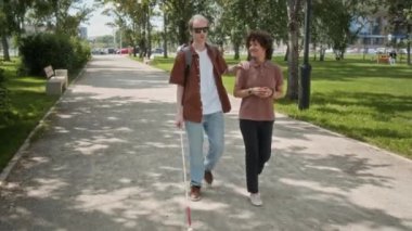 Parkta birlikte yürürken kız arkadaşıyla el ele tutuşan bastonlu görme engelli bir adam.
