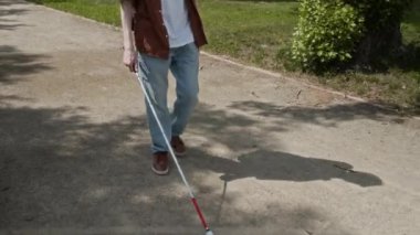 Yaz günü sopayla park yolunda yürüyen görme engelli bir adamın görüntüsünü kaldır.