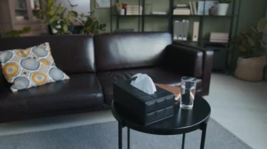 Kimse deri kutuda peçeteler, psikolog ofisinde bir bardak su ve defter, arka planda büyük bir kanepe olan sehpaya bakmaz.