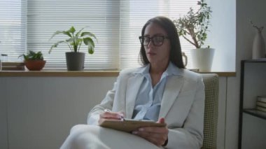 Esmer genç bir kadın terapist. Muayene sırasında müşterisine sorular soruyor ve panoya yazı yazıyor.