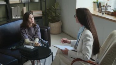 Pantolon giymiş uzun saçlı genç bir terapist. Protezli genç bir kıza danışıyor.