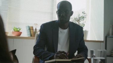 Psikoloji kliniğinde deri koltukta yatan kimliği belirsiz bir kadına danışmanlık yapan Afrikalı Amerikalı erkek terapistin omuz hizasında.