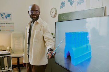 Modern sınıf ortamında 3D baskı sürecini açıklayan Afrikalı Amerikalı eğitimci, görsel yardım için büyük dijital ekran kullanıyor, bilgili ve profesyonel davranış iletiyor