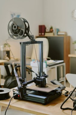 Modern 3D yazıcı organize ofis ortamında gelişmiş teknolojiyi kullanıyor. Aygıt ahşap bir masanın üzerine yerleştirilmiş, ofis malzemeleriyle çevrili bir sonraki baskı görevi için hazır.