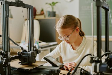 Ofiste 3D yazıcılar tarafından çevrelenmiş yeni bir proje yaratırken kadın mühendis dikkatle dizüstü bilgisayarda çalışıyor. Modern çalışma alanındaki teknoloji ve yeniliğe odaklanın