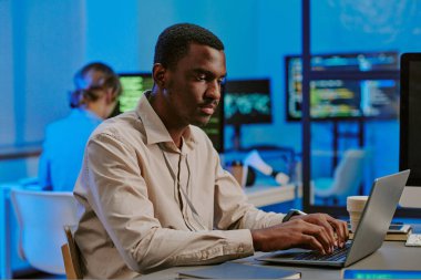 Z jenerasyonunun orta ölçekli görüntüsü, modern ofiste dizüstü bilgisayarda yazan Afrikalı Amerikalı siber güvenlik uzmanı.