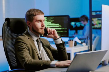 Modern ofisteki bilgisayarlarla uğraşırken genç Kafkasyalı siber güvenlik uzmanının telefonla konuştuğu orta boy bir fotoğraf.