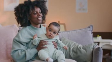 Genç bekar anne oturma odasında yastıklarla kanepede oturuyor ve onu büyütürken ve dizlerinin üstüne çökerken tatlı oğluyla eğleniyor.