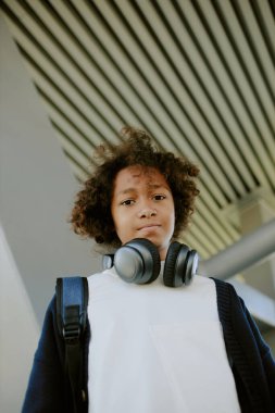 Sıradan kıyafetler giymiş, kameraya bakan modern bir gencin düşük açılı portresi.