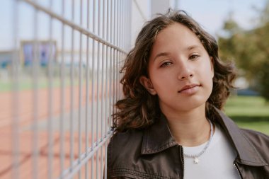 Stadyumun yanında dikilirken sakince kameraya bakan genç kızların orta boy portresi.