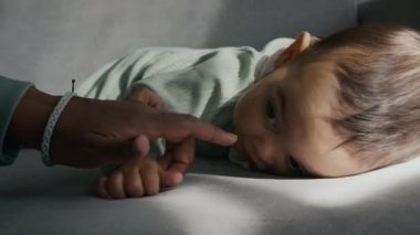 Kadife kanepede sürünen ve tulum giymiş, parmaklarına ve burnuna dokunan, bebekken kameraya bakıp eğlenen Afro-Amerikan bir kadının eli.