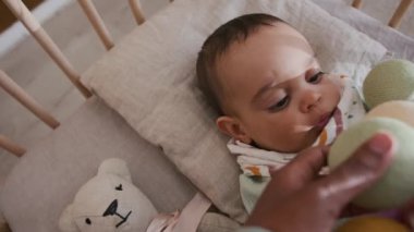 Beşikte uzanmış, beşikte başını yastığa koyan ve farklı renklerde oyuncak toplarıyla oynayan, bekar bir annenin elleriyle sallanan sevimli yeni doğan çocuğun görüntüsünün üzerinde.