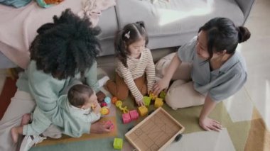 Genç Asyalı bir kadının sarı küpü kızına verip kule inşa ederken her ikisi de Afrika kökenli Amerikalı bir annenin önünde oğluyla otururken.