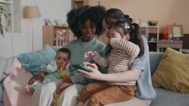 Akıllı telefonlu genç bir Asyalı kanepeye oturmuş küçük kızını dizlerinin üstünde tutarken ona ve sevimli bir oğlu olan Afrikalı Amerikalı bayan arkadaşına internetten ilginç videolar gösteriyordu.