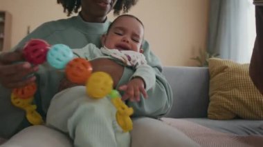 Küçük Asyalı kız yanında oturup anne ve bebeğin fotoğrafını çekerken, mutlu Afrikalı genç bir Amerikalı kadın kanepede oturup ağlayan bebek oğluyla oynuyor.