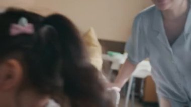 Mavi bluzlu ve bej pantolonlu mutlu bir Asyalı kadın sevimli küçük kızının peşinden koşuyor, gri koltukta minderlerle dolaşıyor, onu yakalıyor, ellerini tutuyor ve gülüyor.