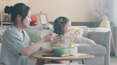 Çizgili kazak giymiş yaramaz küçük kız, annesi kahvaltıda tüm kaşığı yulaf lapasını ya da diğer ev yapımı yemekleri uzatırken başını çeviriyor.