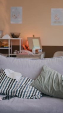 Dikey çekimde, genç Afrikalı Amerikalı kadın, gri koltuğa minderlerle tırmanıyor ve üzerine oturuyor, yeni doğmuş bebeğini dizlerinin üstüne çöktürüyor ve onu yatıştırıyor.