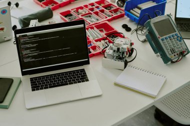 Bilgisayarın yüksek açılı görüntüsü, ekranda kodlar ve çalışma masasının üstünde robot yapmak için detaylar.