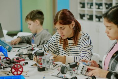 Robot parçaları ve detaylarla dolu bir masada otururken robot prototipini geliştirmeye çalışan konsantre bir kızın orta ölçekli görüntüsü.