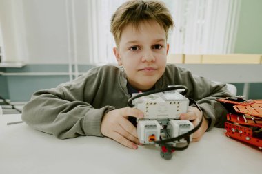 Masada otururken robotun prototipine sarılan sevimli okul çocuğunun orta boy yakın portresi.