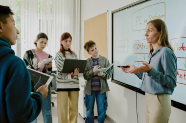 Bilgisayar öğretmeni bir yandan kadın öğrencilerin onu dinlerken ve not alırken konuştuklarını gösteriyor.