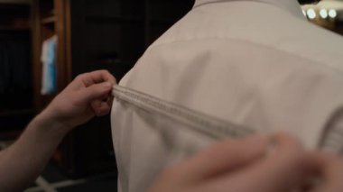 Giysi mağazasındaki erkek müşterinin omuz genişliğini ölçmek için ölçüm bandı kullanılarak tanınmayan kıyafetçinin ellerini kapat