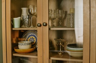 Cam kapılar, gözlük ve renkli tabaklarla donatılmış ahşap bir dolap.