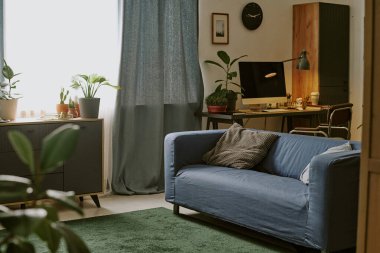 Geniş oturma odası, modern mobilyalar, kil kaplarda bitkiler ve bilgisayarlı çalışma alanı.