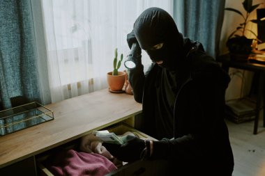 Haneye tecavüz sırasında elinde el feneri olan tanınmamış bir hırsız oturma odasında para paketleri tutuyor.