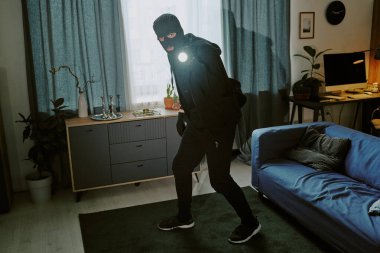 El feneriyle etrafı kolaçan edip eşyaları çalmaya çalışan tanınmamış genç bir hırsız.