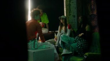 İki çok ırklı arkadaş sohbet ediyor ve birayla şıngırdıyor, genç adam ve kız parti sırasında gülümsüyor ve onları dinliyor.