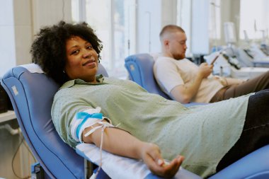 Tıbbi tesiste rahat bir koltukta otururken gülümseyen ve kan bağışı yapan başka bir kişi telefon ederek sırasını bekliyor.