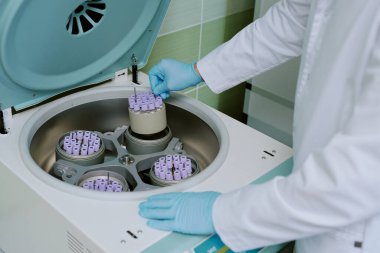 Bilim adamı laboratuvar santrifüj makinesi, koruyucu eldiven takıyor ve test tüpü rafına özenle bakıyor. Çoklu test tüpleri içeren santrifüj pervanesi