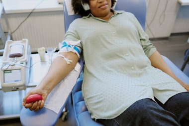 Elinde kan bağışı ekipmanıyla tıbbi bir sandalyede oturan ve kan veren bir kadın. Rahat ve rahat bir tıbbi tesiste, iyi bir amaca hizmet ediyor.