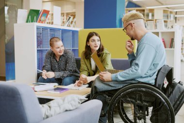 Modern kütüphanedeki çalışma oturumunda fikir üreten ve projeleri tartışan bir grup öğrenci raflar dolusu kitap ve onları çevreleyen çeşitli oturma düzenleriyle