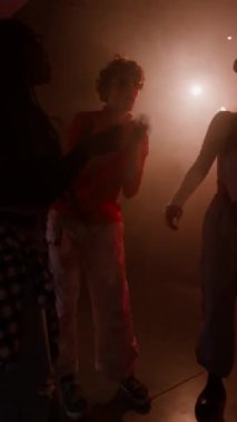 Neon ışıkları ve yanıp sönen ışıklarla dans pistinde parti müziğinin keyfini çıkaran çok ırklı Z jenerasyonundan bir grubun dikey çekimi.