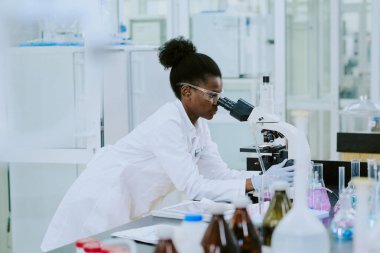 Güvenlik teçhizatı ve mikroskopla gözlemleyen beyaz laboratuvar önlüğü giyen bilim adamları laboratuvarda çeşitli bilimsel ekipmanlar ve kimyasal çözümlerle çevrili araştırmalar yürütüyorlar.