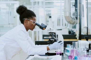 Laboratuvarda mikroskop kullanarak numuneleri inceleyen bilim adamları steril ortamda çeşitli ekipman ve test tüpleriyle araştırma yapıyorlar.