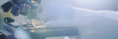 Laboratuvar çalışanı, küçük bir örneğin detaylı analizi için yüksek hassasiyetli mikroskop kullanıyor. Çevre steril ve gelişmiş ekipmanlarla aydınlık görünüyor
