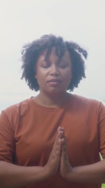 Çok ırklı olgun bir kadının parkta ya da ormanda yoga yaparken meditasyonla rahatlamasının dikey çekimi.