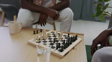 Evdeki oturma odasındaki küçük sehpada oynarken iki Afrikalı Amerikalı adamın teknede satranç taşlarını taşırken yakın plan çekimleri.