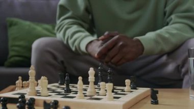 Kanepeye oturup satranç tahtasına bakan konsantre Afro-Amerikan bir adamın evde becerilerini geliştirirken oyun stratejisini derinden düşünmesini çek.