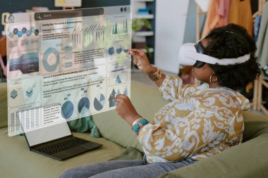 Oturma odasındaki sanal elementlerle etkileşime girerken VR kulaklık takan siyah bir kadın.