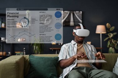 VR kulaklık takan genç siyahi bir adam oturma odasında kanepede oturmuş sanal klavyeye yazı yazıyor.