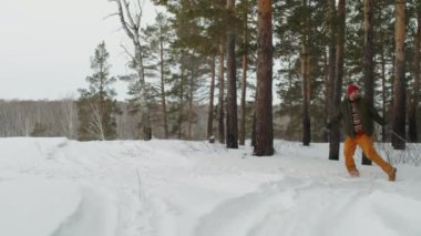 Bir adam koşuyor ve kız arkadaşını kızakla yokuş yukarı çekiyor, karlı ormanda kar yığınları ve yemyeşil ağaçların arasında yürürken mutlu bir şekilde gülümsüyor.